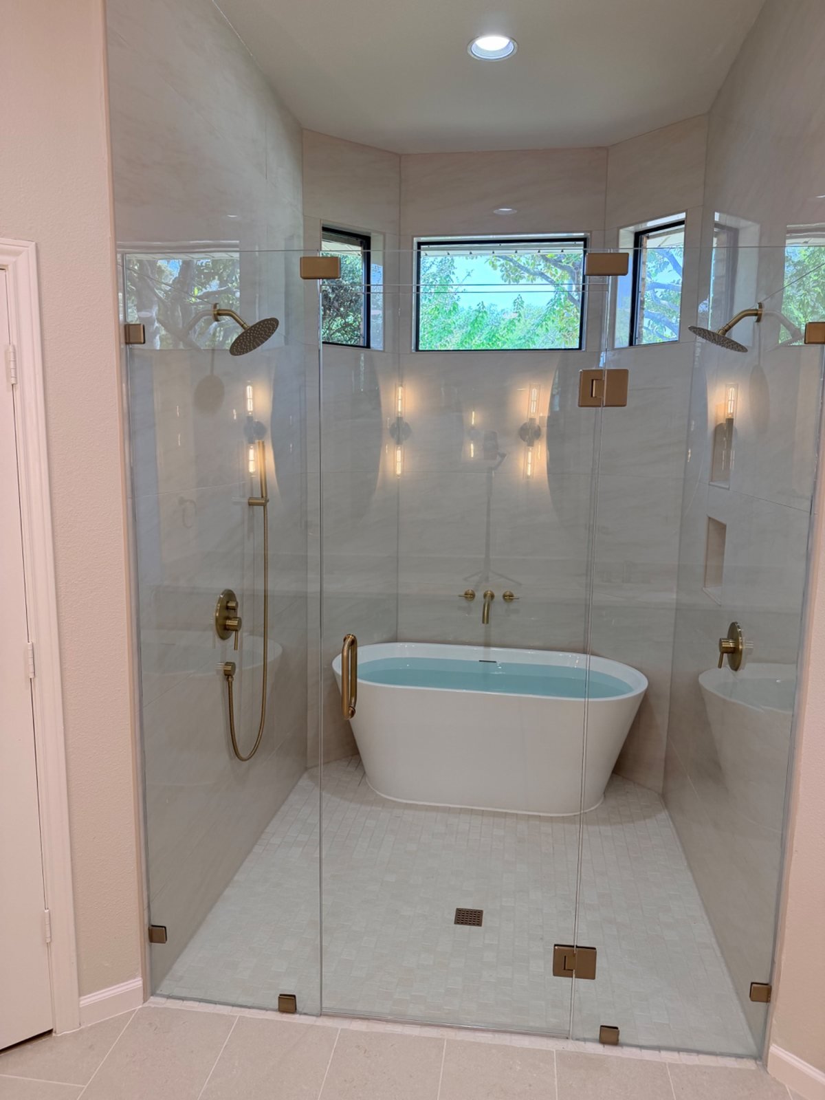 CJJ bathroom with a freestanding tub inside a glass shower, twin showerheads and brass finishes